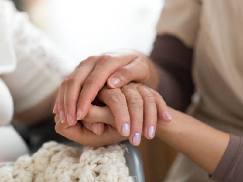 Close-up photo of a female caregiver and senior woman holding hands. Senior care concept.